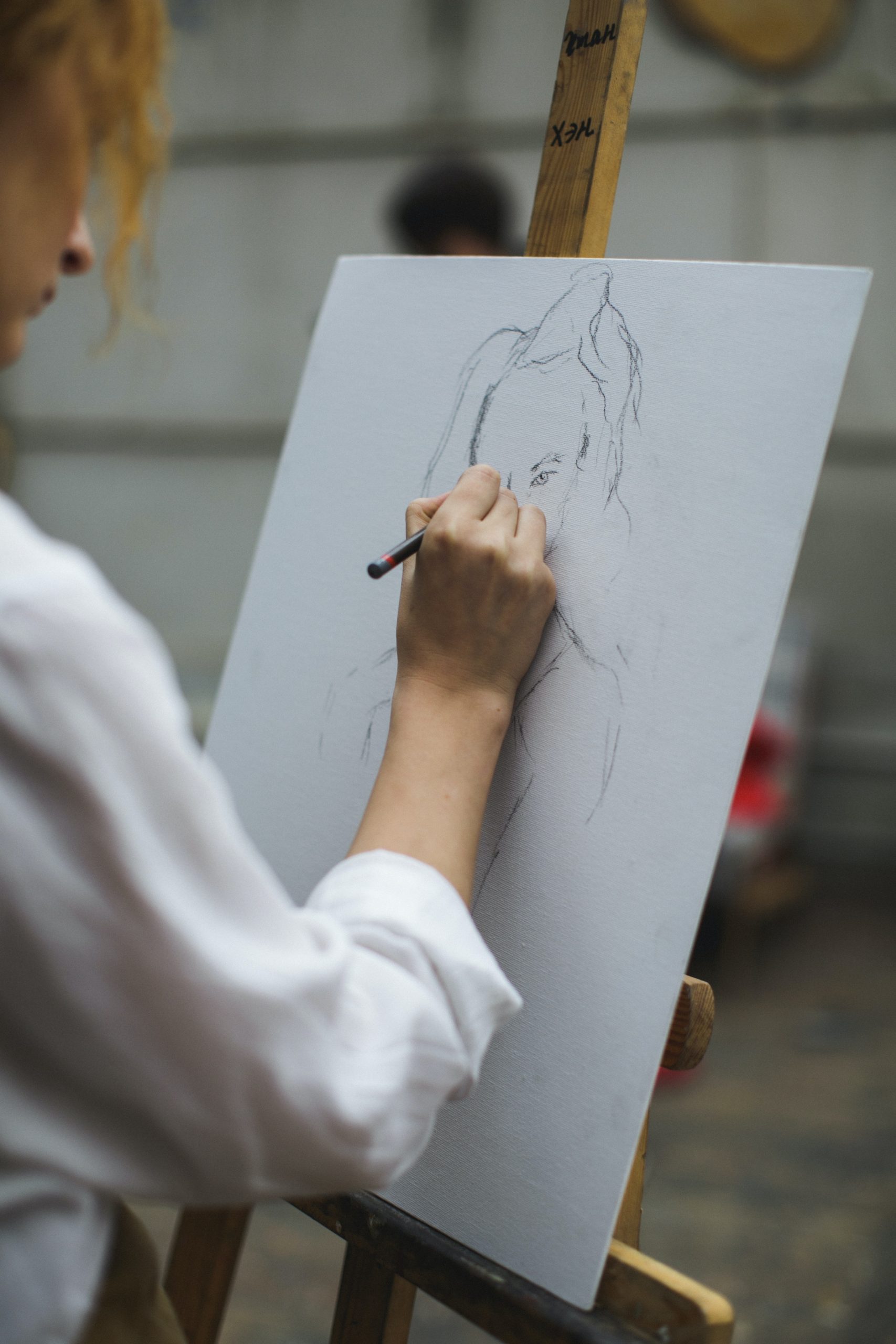 A woman draws a portrait of another person in fine detail.