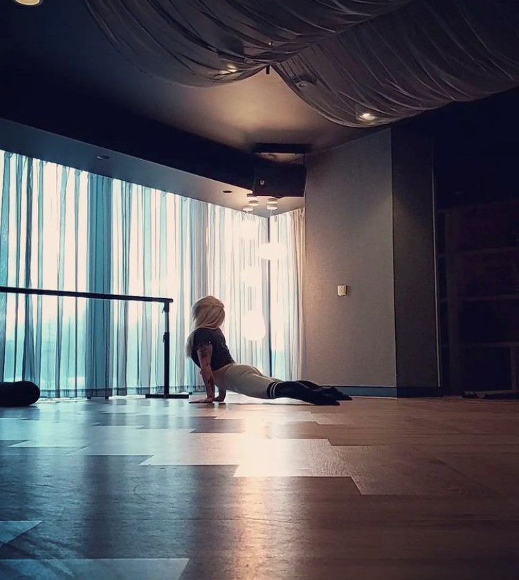 Kate Tittley - Yoga in a dark, but well lit room, with floor to ceiling windows.