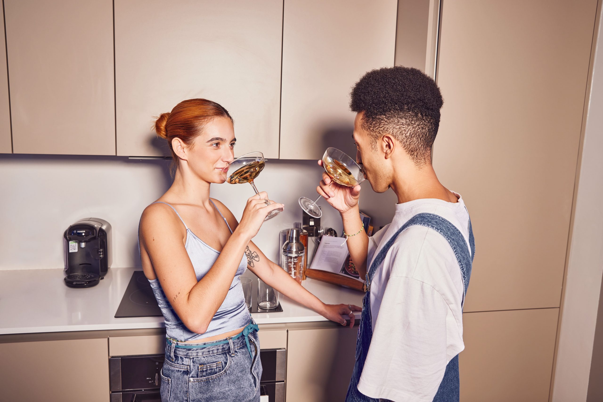 Two young people drink from high-quality glasses in a modern kitchen.